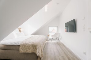 A modern bedroom with a bed, a TV, a chair, and a window. - de See - Suite 4 Seitliche Deichlage (Greetsiel)