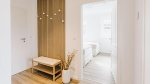 A hallway with a wooden bench, a white vase with branches, and a door leading to a bedroom. - de See - Suite 4 Seitliche Deichlage (Greetsiel)