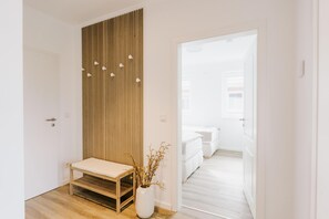 A hallway with a wooden bench, a white vase with branches, and a door leading to a bedroom. - de See - Suite 4 Seitliche Deichlage (Greetsiel)