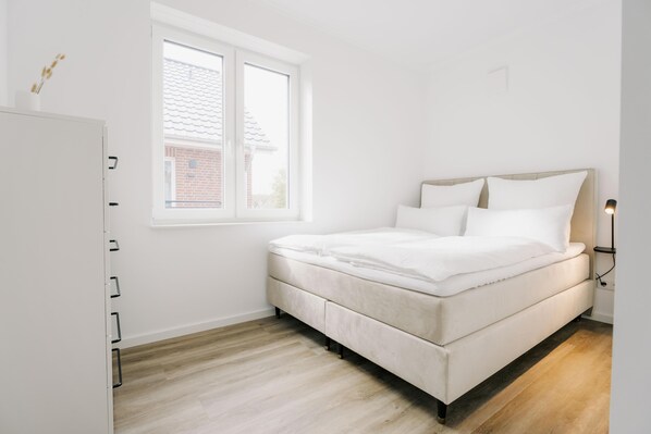 A bedroom with a bed, a window, a white wardrobe, and a bedside lamp.