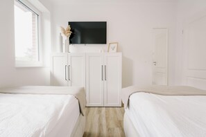 Un dormitorio con dos camas, televisor, armario y ventana.