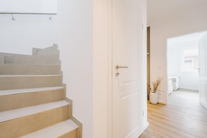 Eine Treppe führt zu einem Raum mit einer weißen Tür, einer Zimmerpflanze und Blick ins Badezimmer.