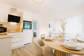 Una cocina moderna con armarios blancos, microondas integrado y estufa. Cuenta con un comedor con una mesa redonda preparada para cuatro personas, con platos y vasos blancos.