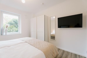 Un dormitorio con cama, ventana, armario y televisor instalado en la pared.