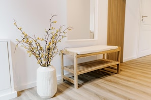 Un jarrón blanco con flores amarillas, un banco de madera y una puerta blanca en una habitación con suelo de madera clara.