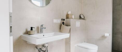 A modern bathroom with a white sink, toilet, and a round mirror.