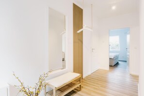 Un intérieur moderne avec un banc en bois, un miroir et une porte donnant sur une chambre à coucher.