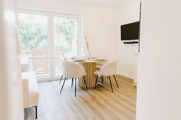 A modern dining area with a round table, white chairs, and a large window.