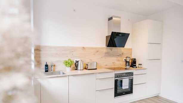 Una cocina moderna con armarios blancos, un salpicadero de madera, horno empotrado y cafetera.
