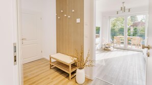 Un interior moderno con un banco de madera, un jarrón blanco con ramas y vistas a un patio exterior con sillas.