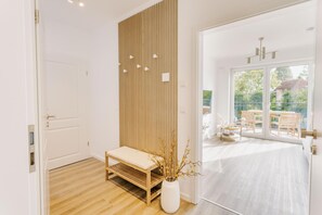 Ein modernes Interieur mit einer Holzbank, einer weißen Vase mit Zweigen und Blick auf eine Terrasse mit Stühlen.