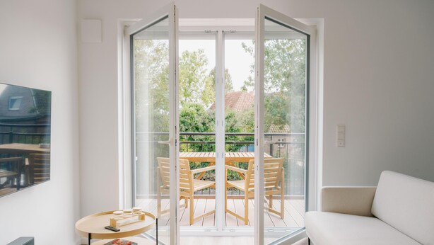 A modern living room with a sofa, a round table, and a balcony with a wooden table and chairs. - de See - Suite 2 Direkte Deichlage (Greetsiel)
