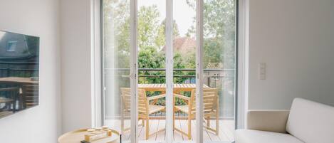 Een moderne woonkamer met een bank, een ronde tafel en een balkon met een houten tafel en stoelen.