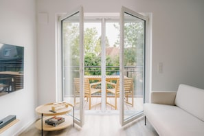 Ein modernes Wohnzimmer mit einer Couch, einem runden Tisch und einem Balkon mit Holztisch und Stühlen.