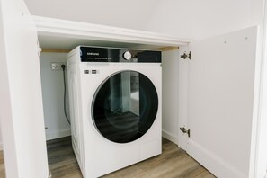 Eine kompakte, weiße, an der Wand befestigte Waschmaschine in einem kleinen Waschraum mit Holzboden.