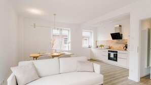 Una cocina moderna con armarios blancos, horno empotrado y comedor con mesa y sillas.