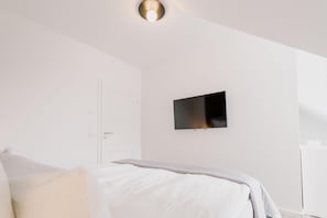 Ein schlicht eingerichtetes Schlafzimmer mit einem Bett, einem an der Wand befestigten Flachbildfernseher und einer Tür.
