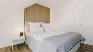 Un dormitorio con una cama, una mesita de noche, una lámpara y cabecera de madera con listones.