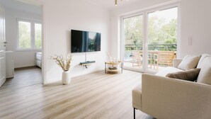 Una sala moderna con una televisión de pantalla plana, un sofá, una mesa de centro y un amplio ventanal corredero que da a un espacio exterior.