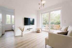 Una sala moderna con una televisión de pantalla plana, un sofá, una mesa de centro y un amplio ventanal corredero que da a un espacio exterior.