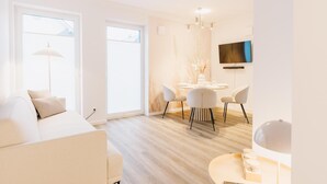 A modern living room with a sofa, dining table, chairs, and a TV. - de Diek - Suite 3 Seitliche Deichlage (Greetsiel)