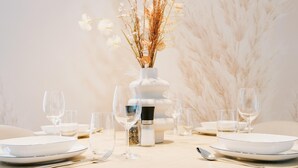 A round dining table with white plates, clear glasses, and cutlery. A white vase with dried flowers is centered on the table. - de Diek - Suite 3 Seitliche Deichlage (Greetsiel)