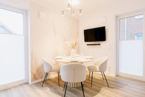 A modern dining area with a round table, white chairs, and a flat-screen TV mounted on the wall.