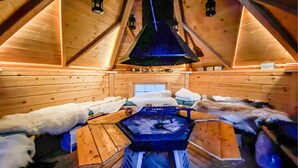 A log cabin with a central fireplace, wooden benches, and fur-covered seating. - Nice home in Gol with kitchen (Gol)