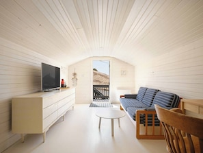 A cozy room with a TV, sofa, wooden chair, and a small table.