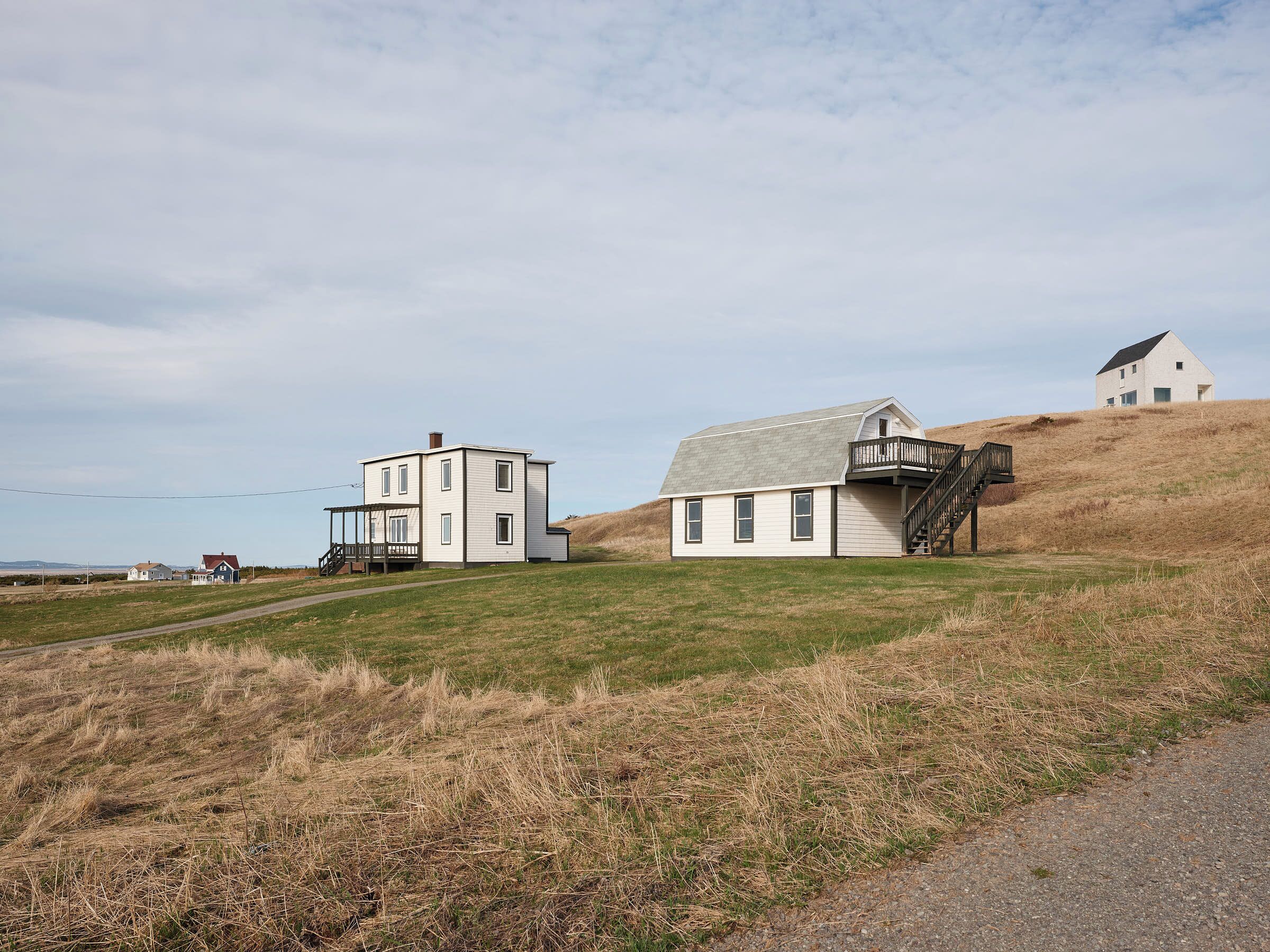 Et moderne hus med to etager, en overdækket veranda, en trappe op til en balkon og en separat bygning på en bakke.