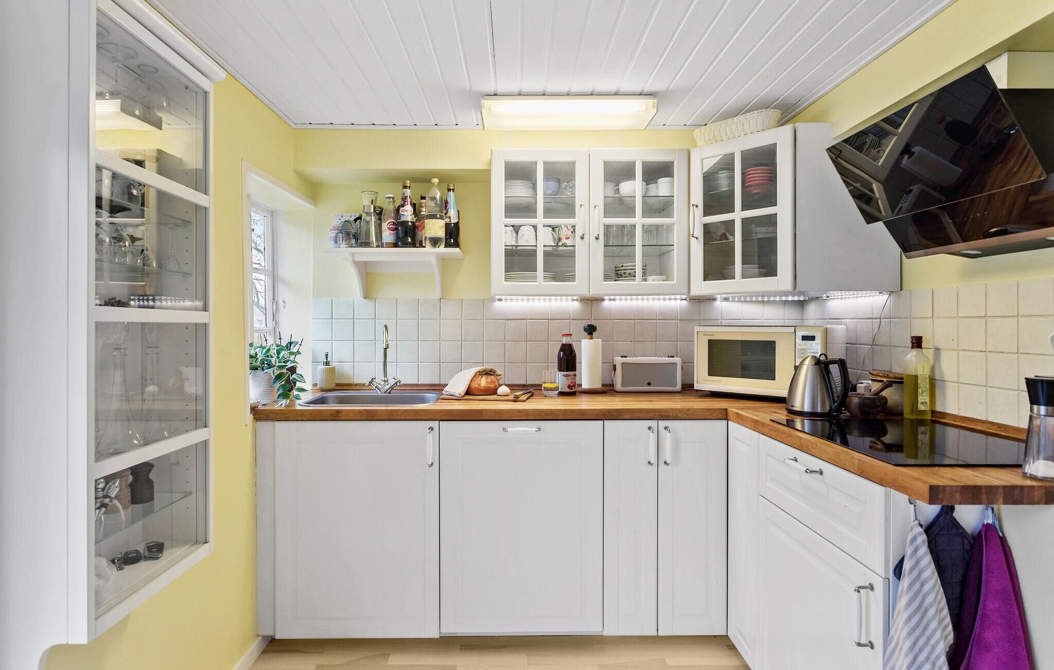 A kitchen with white cabinets, a microwave, a kettle, and various kitchen items on the counter.