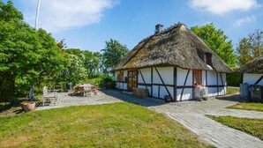 A traditional thatched-roof house with a white and black timber frame, a red door, and a small window.