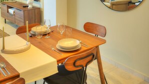 A dining area with a wooden table set for four, a round mirror on the wall, and a view into the living room through the mirror. - Luxury&stylish 2bedroom seafront, balcony GOGZR-4 (Gzira)