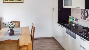 Une cuisine avec une table à manger en bois, des chaises, un vase de fleurs, un plan de travail noir, un évier et une cuisinière.