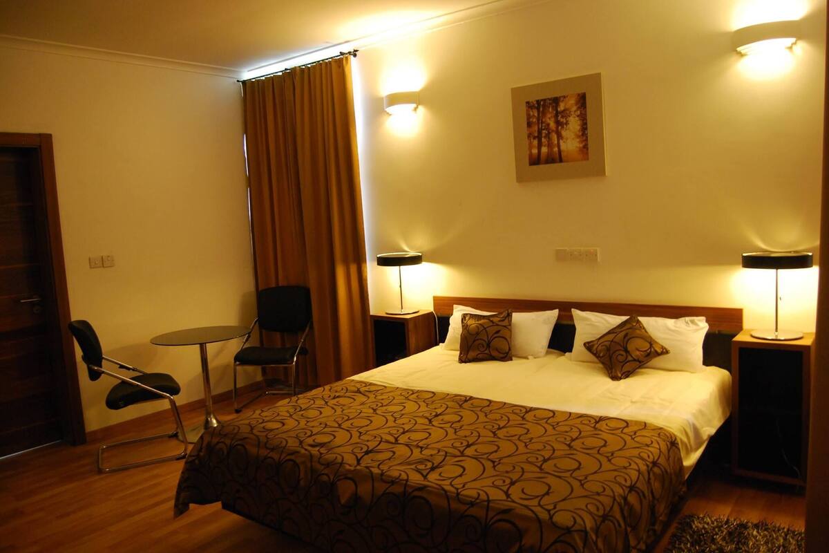 A hotel room with a large bed, two bedside tables, a chair, and a small table.
