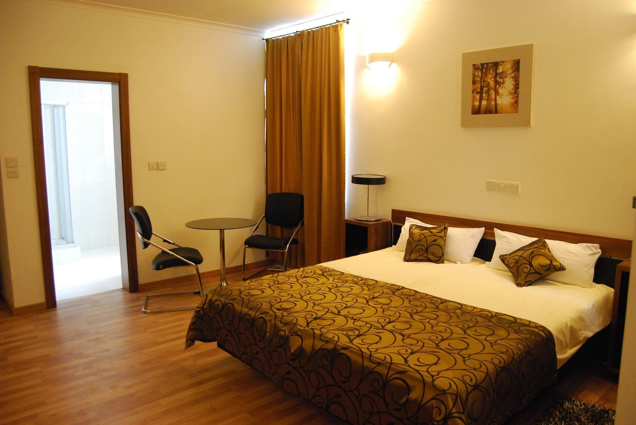 A hotel room with a bed, a chair, a small table, and a curtain.