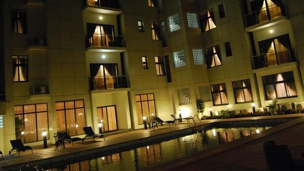 A multi-story hotel with a pool area, outdoor seating, and illuminated windows. - Pearl Court Residence & Hotels (Lagos)