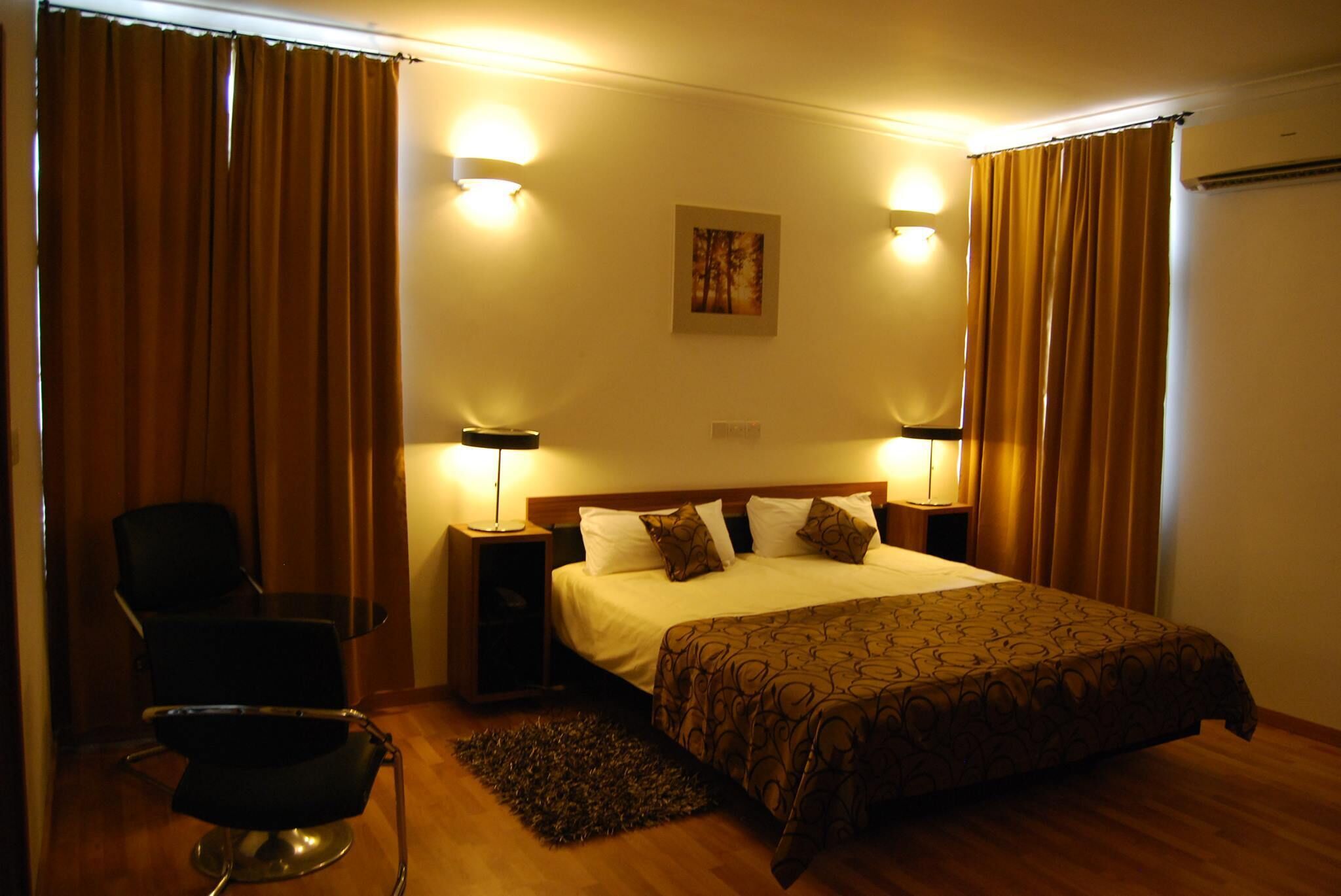 Una camera d'albergo con un letto, due lampade da comodino, una sedia e un tappeto.