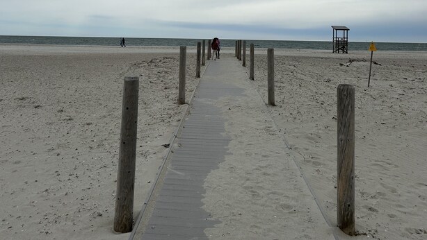 Uma trilha de concreto leva a uma torre salva-vidas em uma praia arenosa.
