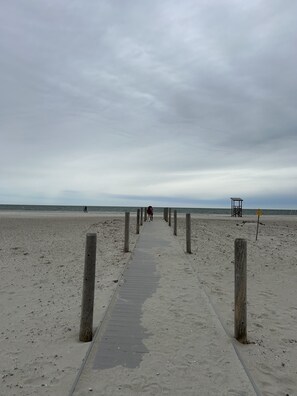 Een betonnen pad dat naar een bewakingspost op een zandstrand leidt.