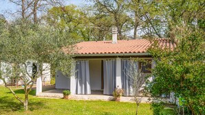 A small, single-story house with a tiled roof, a covered porch, and a garden area with grass and trees. - Gorgeous home in Valbandon with WiFi (Valbandon)