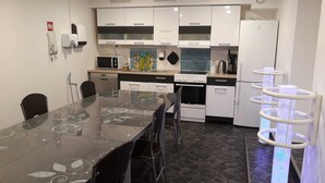 Una cocina moderna con armarios blancos, una mesa de comedor de vidrio y una lámpara de techo original.