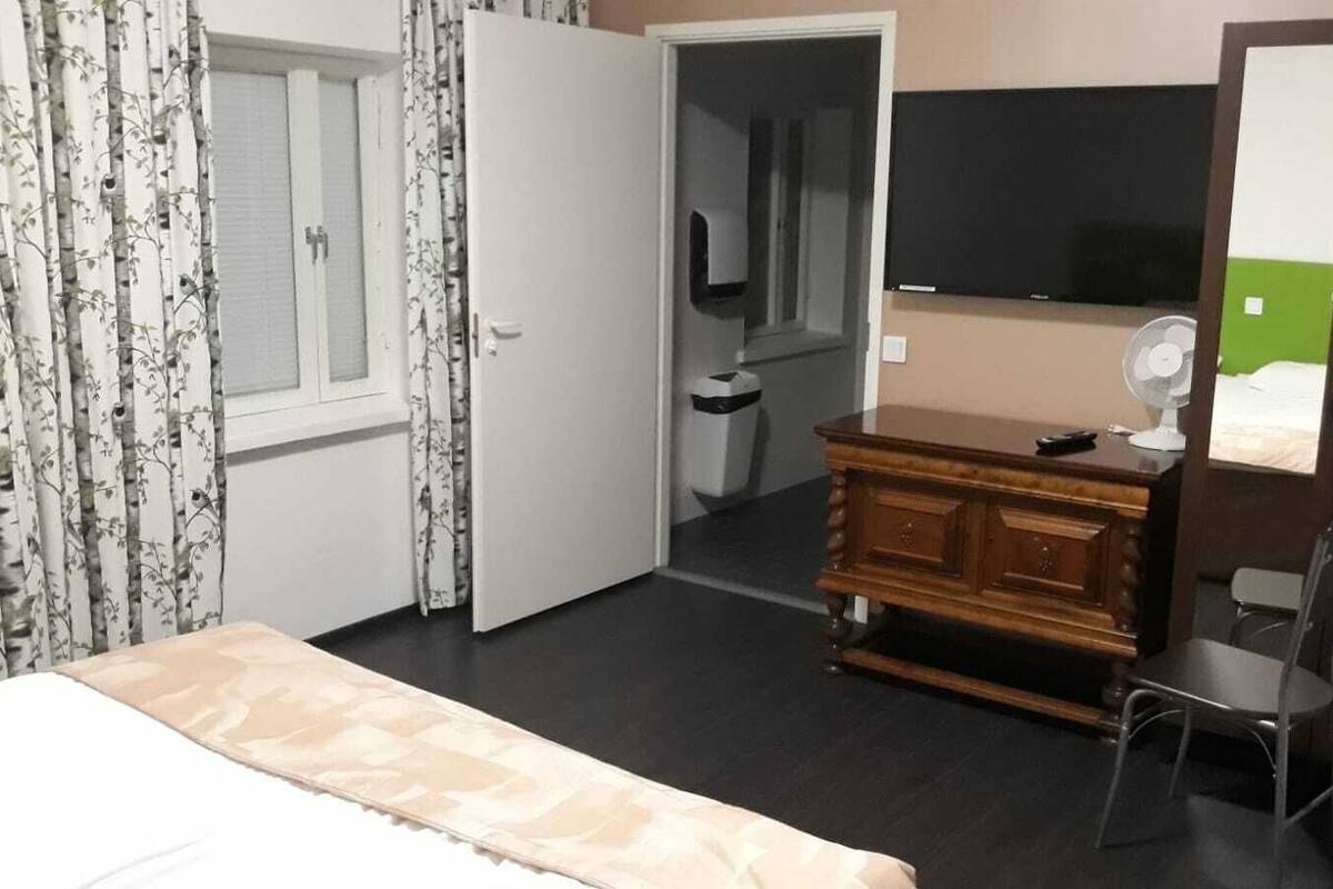 A hotel room with a bed, a wooden dresser, a chair, a mirror, and a television.