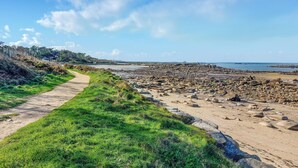 Un sentier côtier bordé d’une plage rocheuse et offrant une vue dégagée sur la mer.