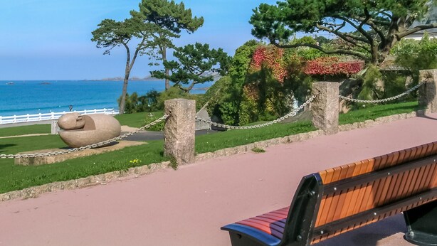 Un banc installé le long d’une allée pavée, offrant une vue sur l’océan et agrémenté d’une sculpture en pierre.