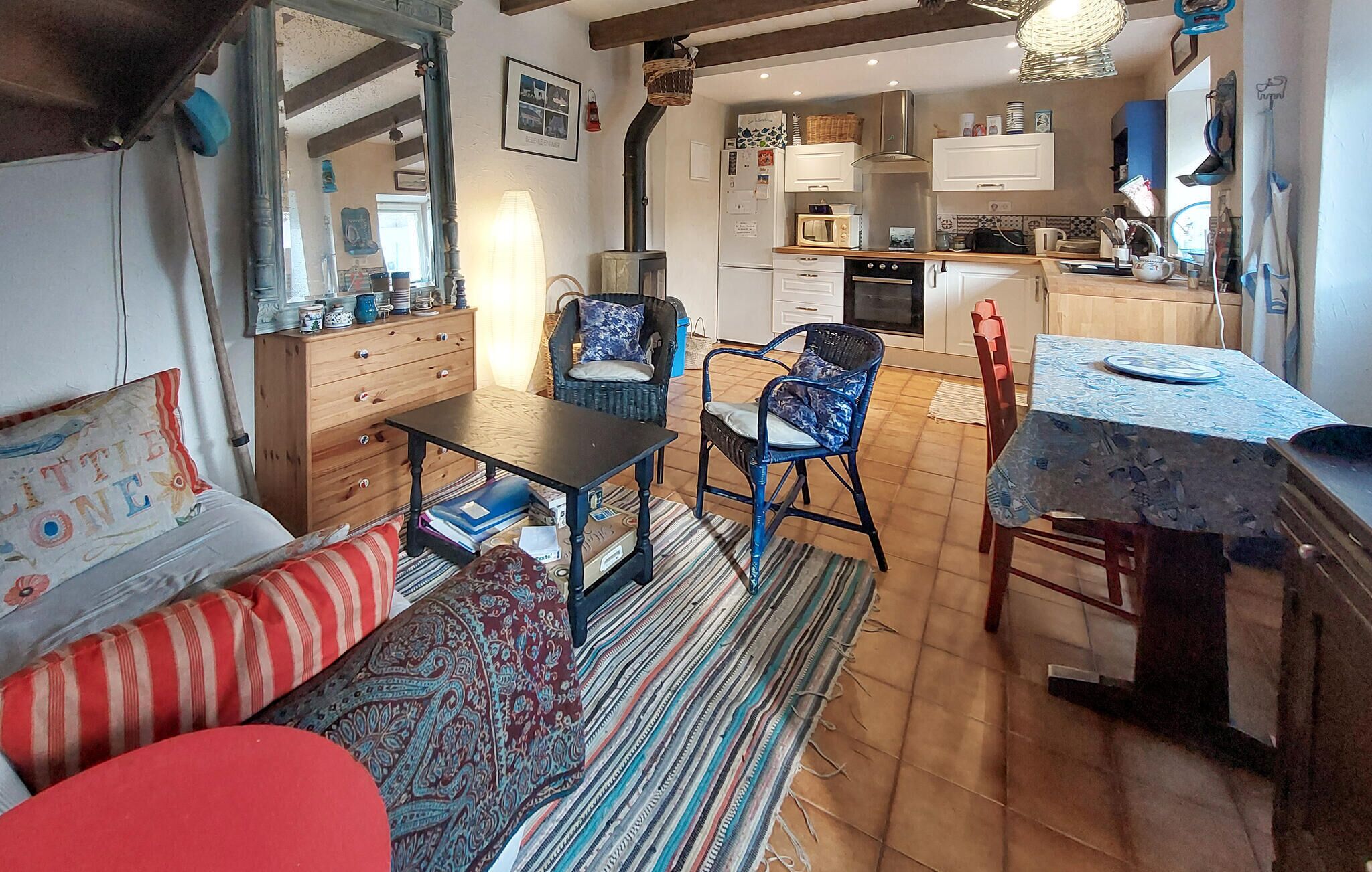 Un salon chaleureux avec un canapé, des fauteuils, une table à manger et une cuisine en arrière-plan.