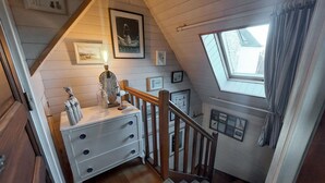 Un escalier avec une rampe en bois, une commode blanche à tiroirs et une lucarne au-dessus.