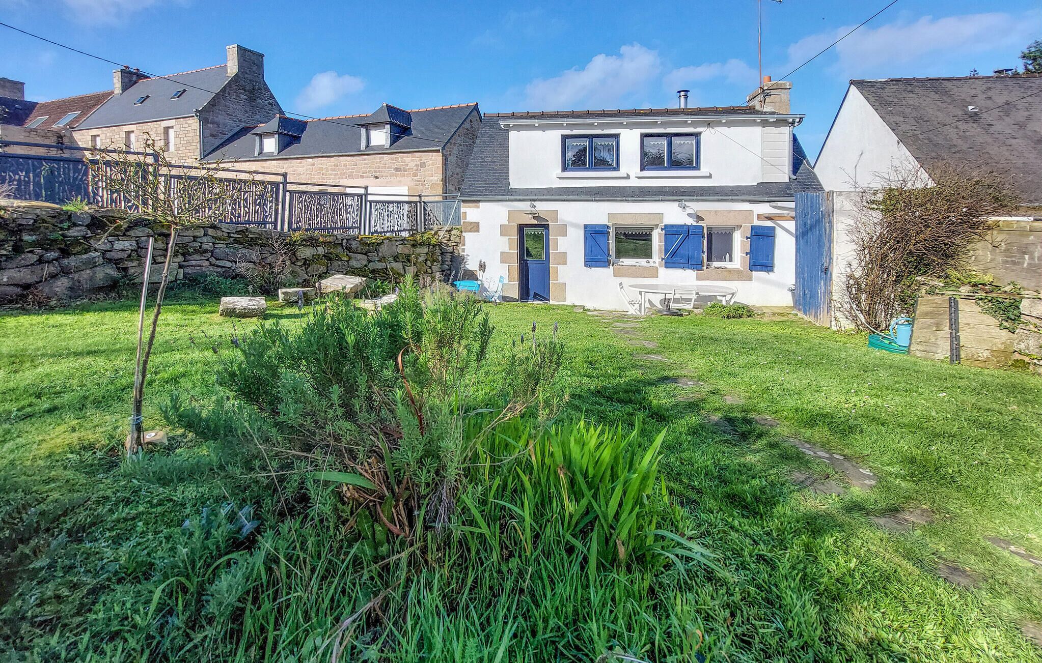 A two-story house with a stone facade, a small garden, and a blue door.