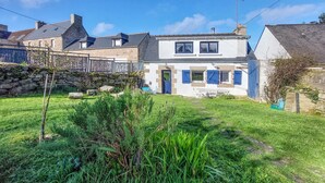 Une maison à deux étages avec une façade en pierre, un petit jardin et une porte bleue.