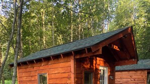 A small wooden cabin with a porch, surrounded by gravel and greenery. - Taborton Harvest Timber Trails
Unique cabin experience (Sand Lake)